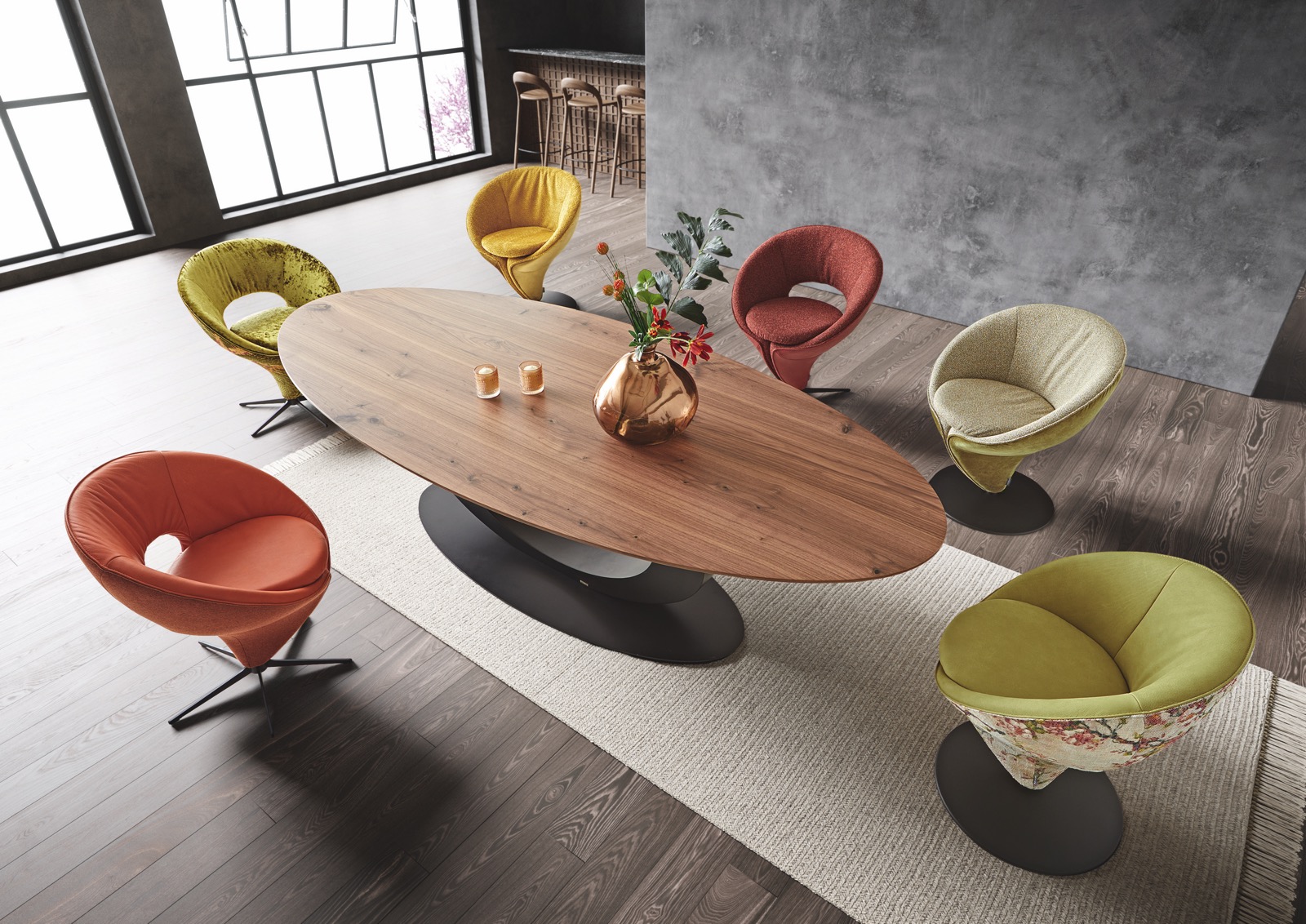 A picture of a dining room with multicolored elegant chairs around an oval walnut-topped dining table